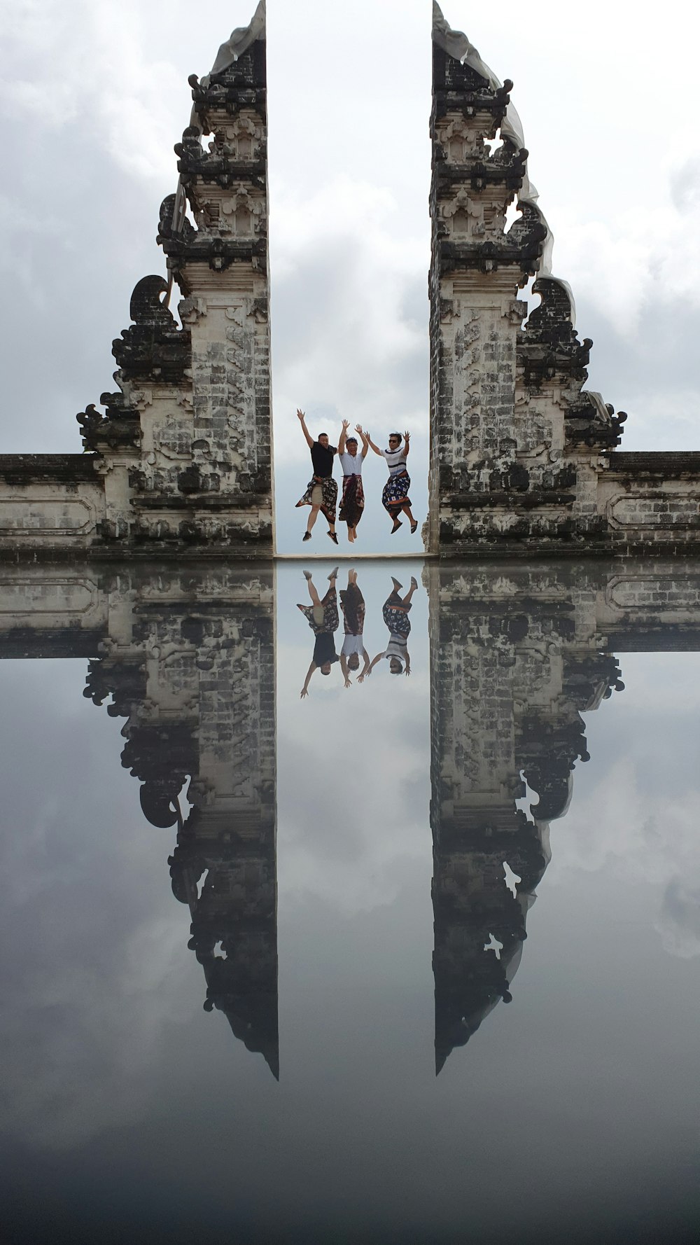 three person jumping near calm water