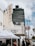 A street scene featuring a vintage theater marquee at the El Rey, displaying information for Zoe Church LA. People mill about under white tents that suggest an event or market. The background shows a tall black office building with the number 5455 and palm trees lining the street.