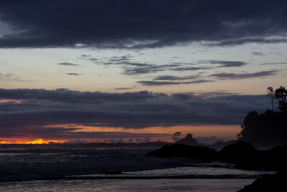 the sun is setting over the ocean on a cloudy day