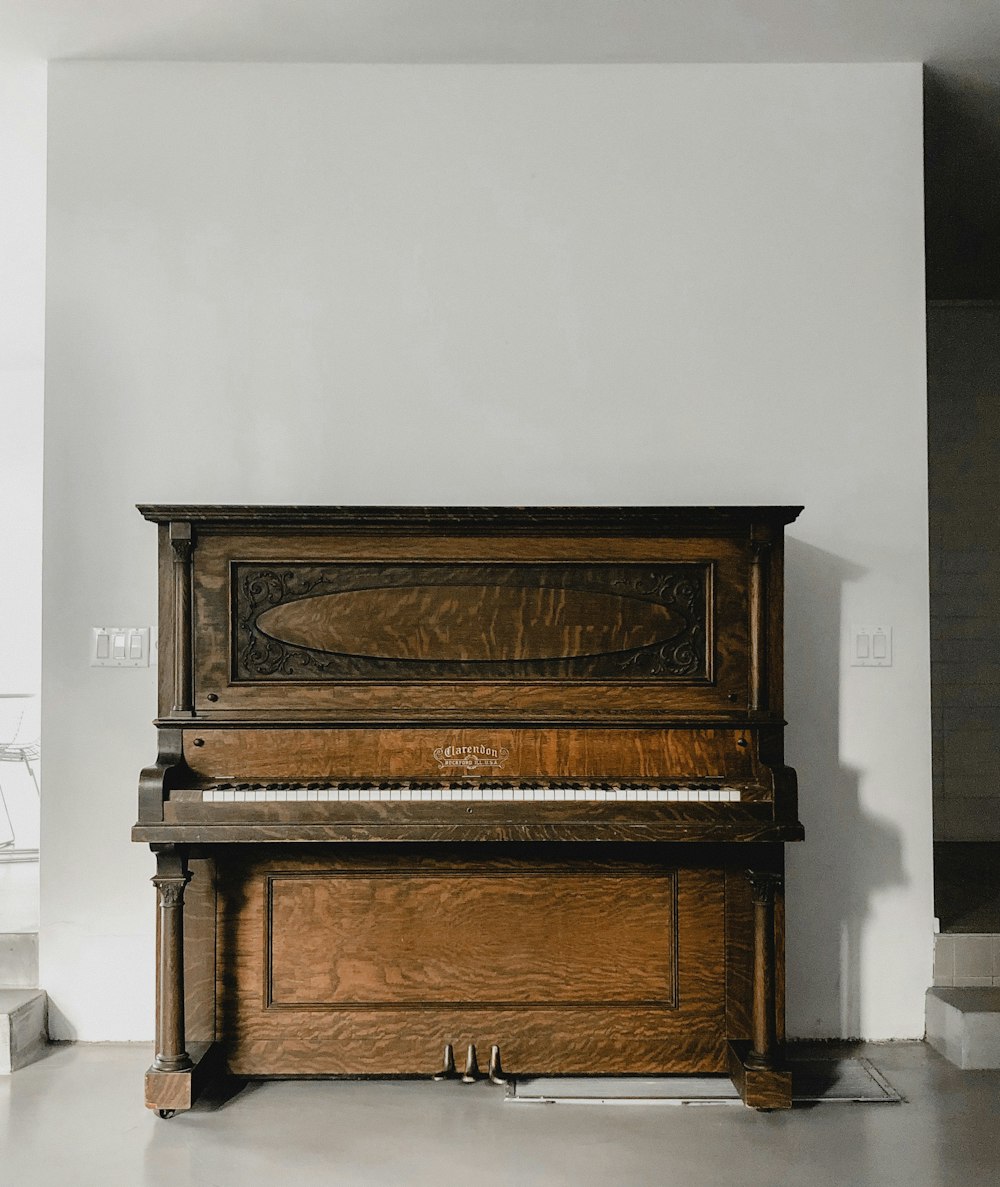 白い壁の横の茶色の木製のアップライトピアノ
