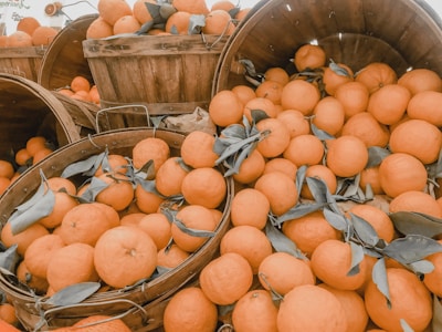 Bright oranges arranged in a rustic wooden box with leaves.