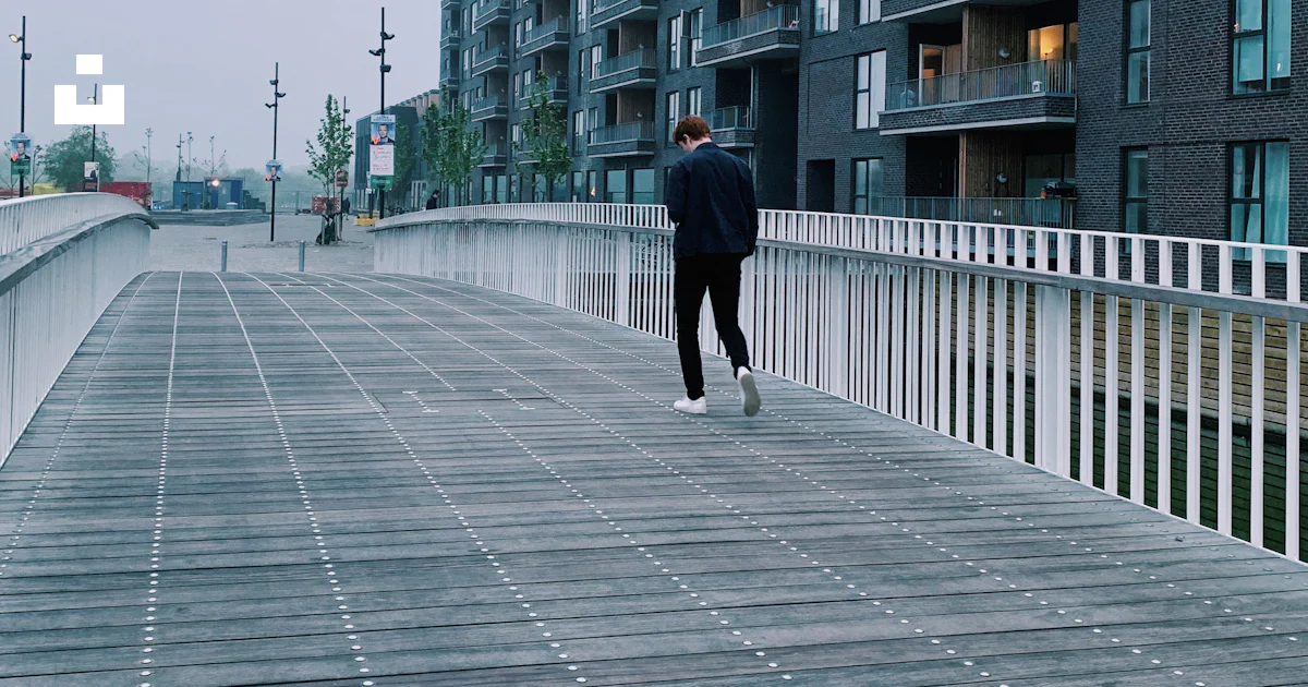 Man walking alone on pathway looking down beside high-rise buildings ...