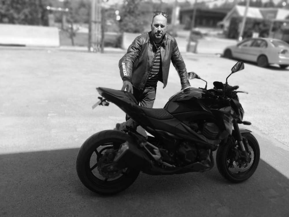 grayscale photo of man standing beside parked naked sports motorcycle