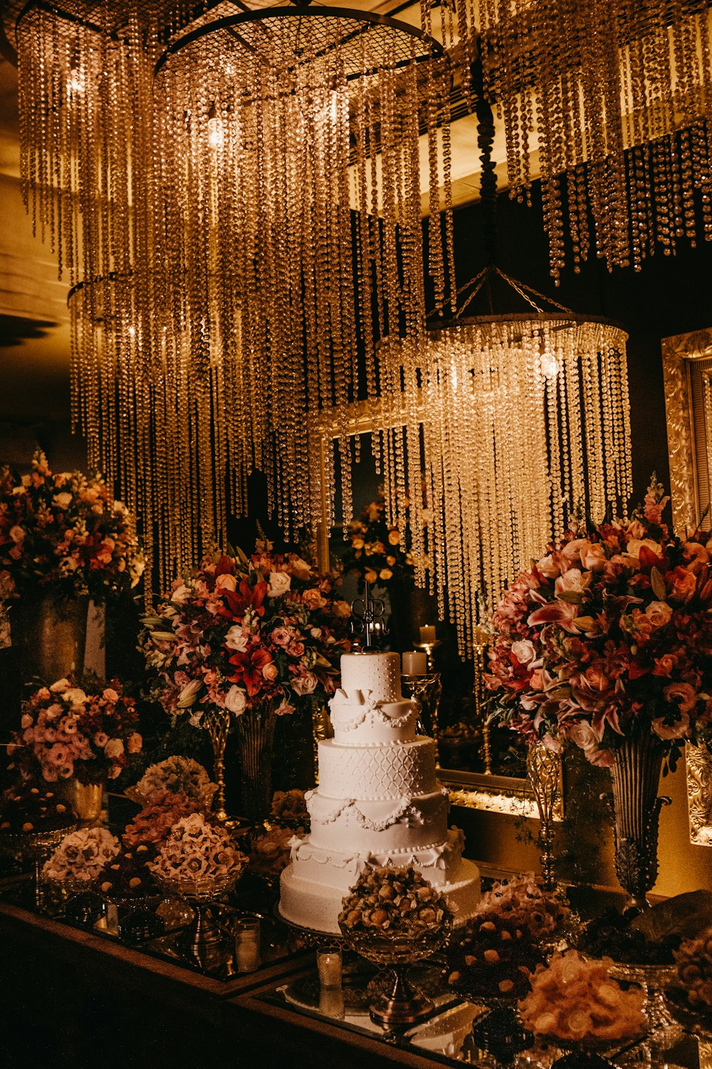 5-stöckige Hochzeitstorte, umgeben von verschiedenfarbigem Blumenarrangement mit beleuchteten Kronleuchtern