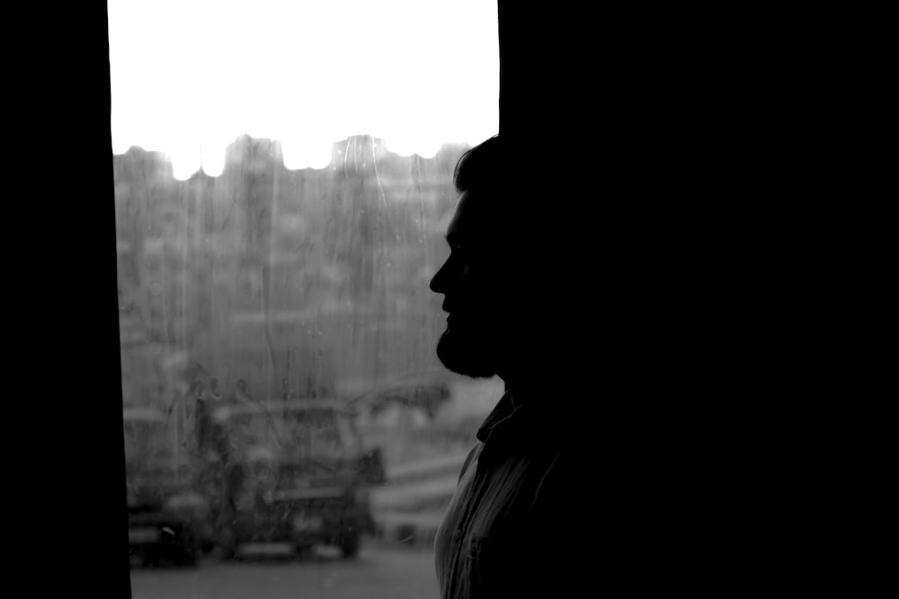 a black and white photo of a person looking out a window