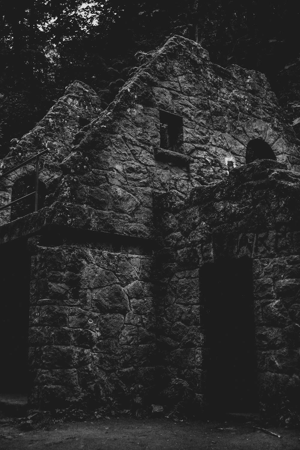 grayscale photo of stone house surrounded with trees