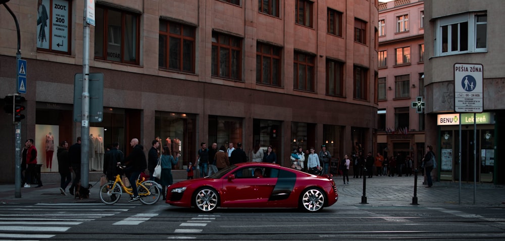 red sedan on road near people walking beside concrete buildings