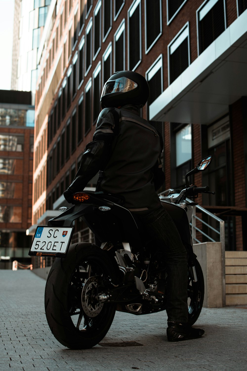 person sitting on black motorcycle near brown concrete building