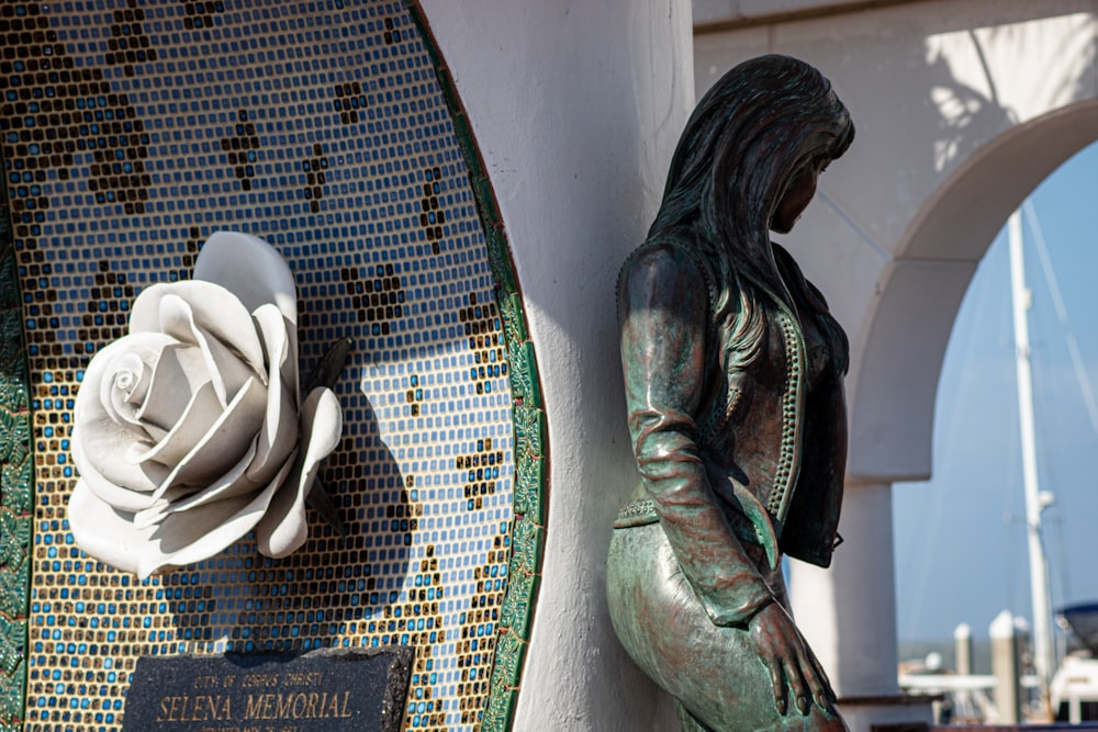 Una estatua de una mujer junto a una rosa blanca