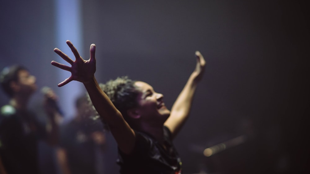 woman standing and smiling while raising both hands surrounded with people