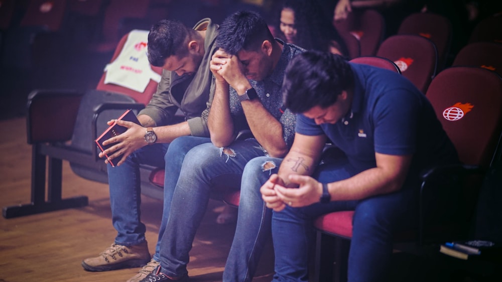 three men sitting on individual chairs closing there eyes and praying