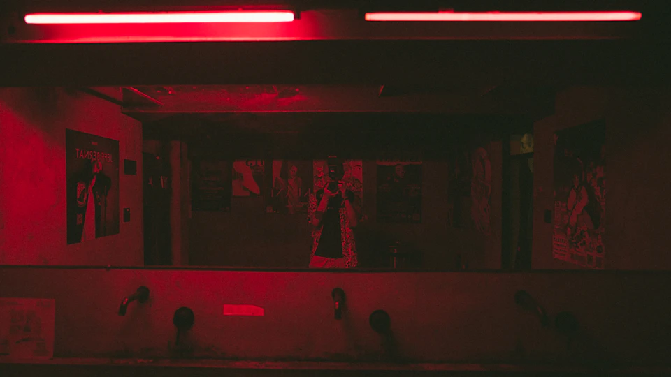 Dimly lit room with two red lights and white walls featuring multiple posters