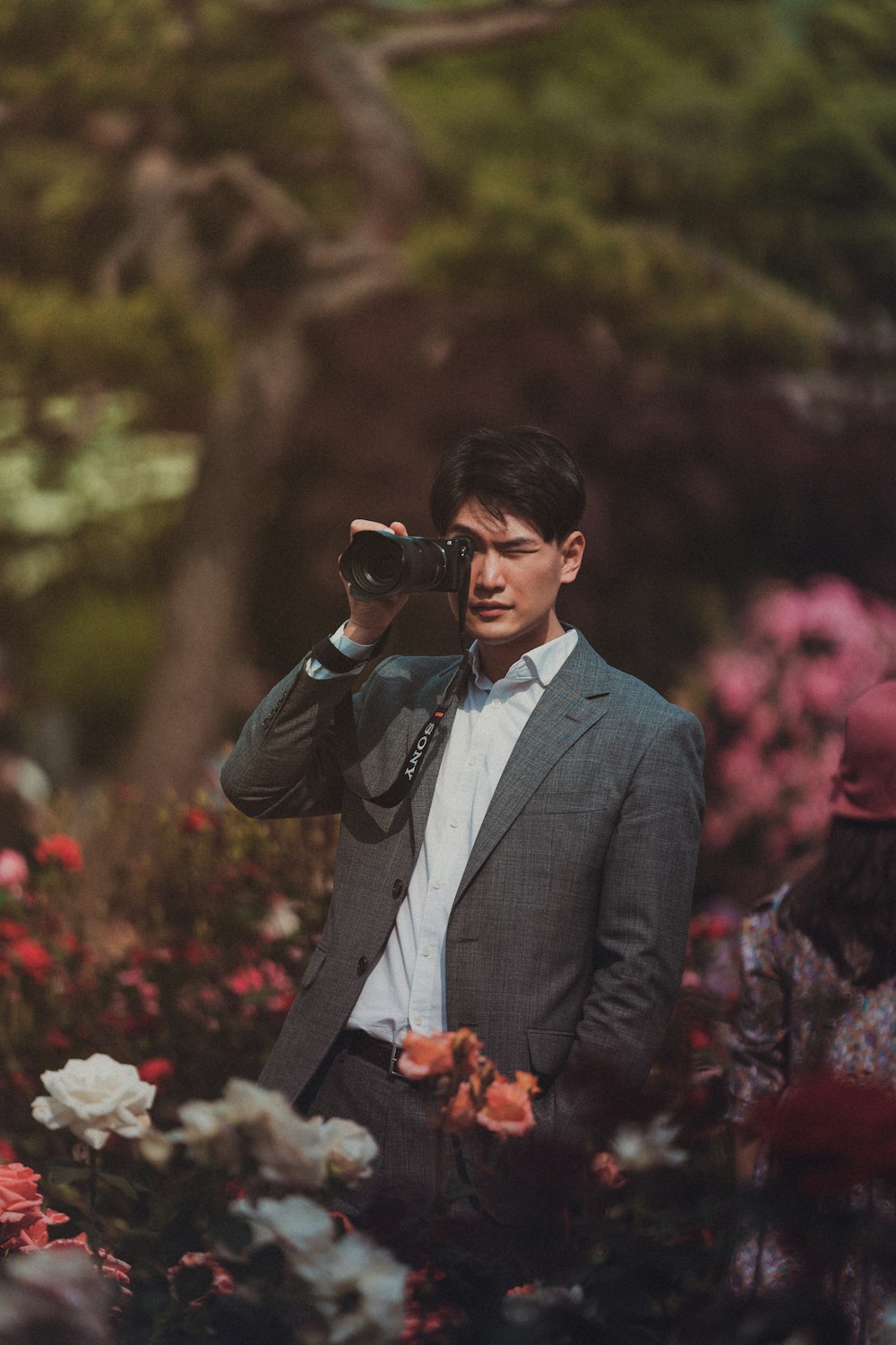 uomo in piedi e usando la fotocamera DSLR nel mezzo del giardino fiorito