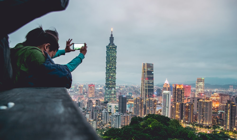 person who holding smartphone taking photo of Taipei 101 during daytime