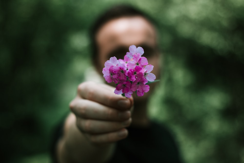 man holding bunch of small pink flowers