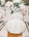 A detailed wedding table setup with white plates and a wedding menu placed on one of them. The table is decorated with elegant floral arrangements and champagne glasses with striped gold stems. Silverware is neatly placed on either side of the plates.
