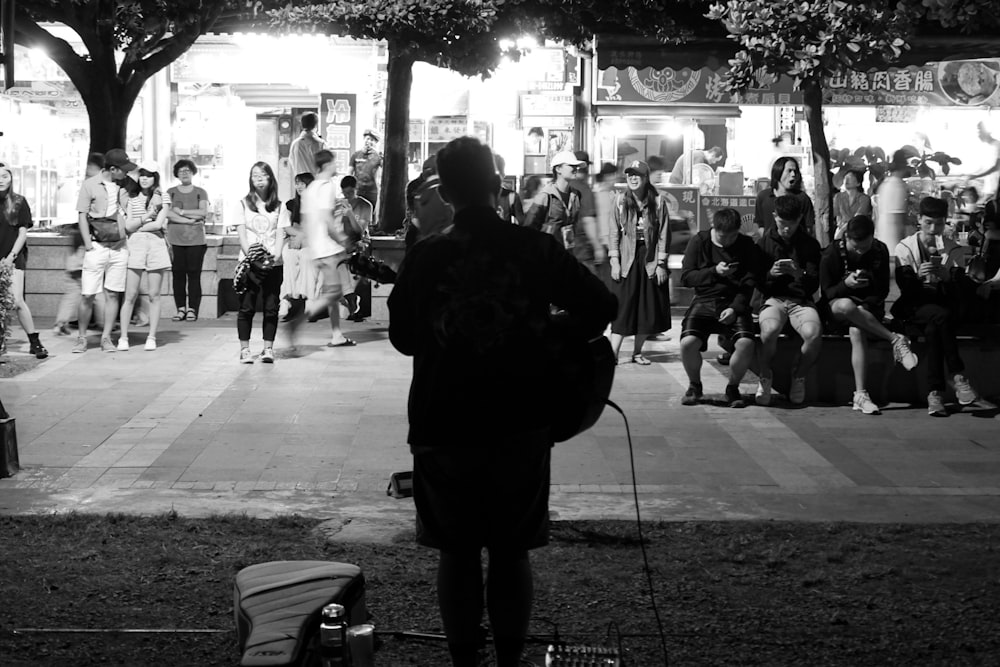 grayscale photo of person playing guitar on street