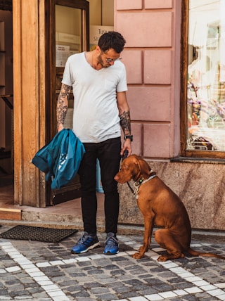 man standing beside sitting dog near open door of building