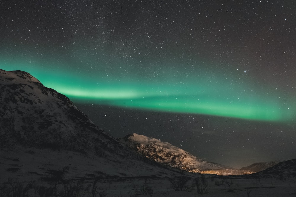 snow covered hill under green starry sky