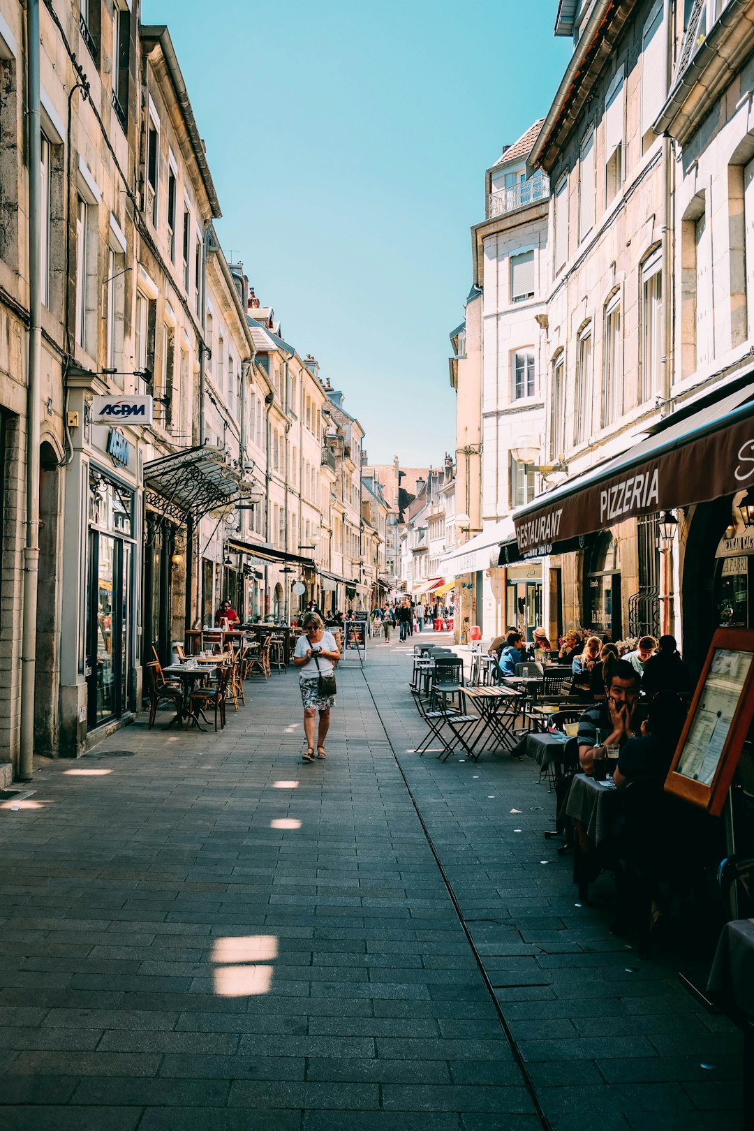 person walking on alleyway with restaurant tables during daytime