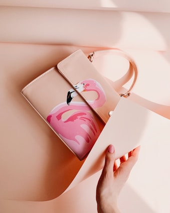 A pastel pink-themed aesthetic photo featuring a stylish handbag resting on a soft fabric background.