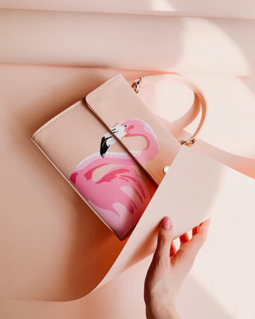 Close-up of a stylish olive green handbag with delicate pink accents, resting on a white textured surface.