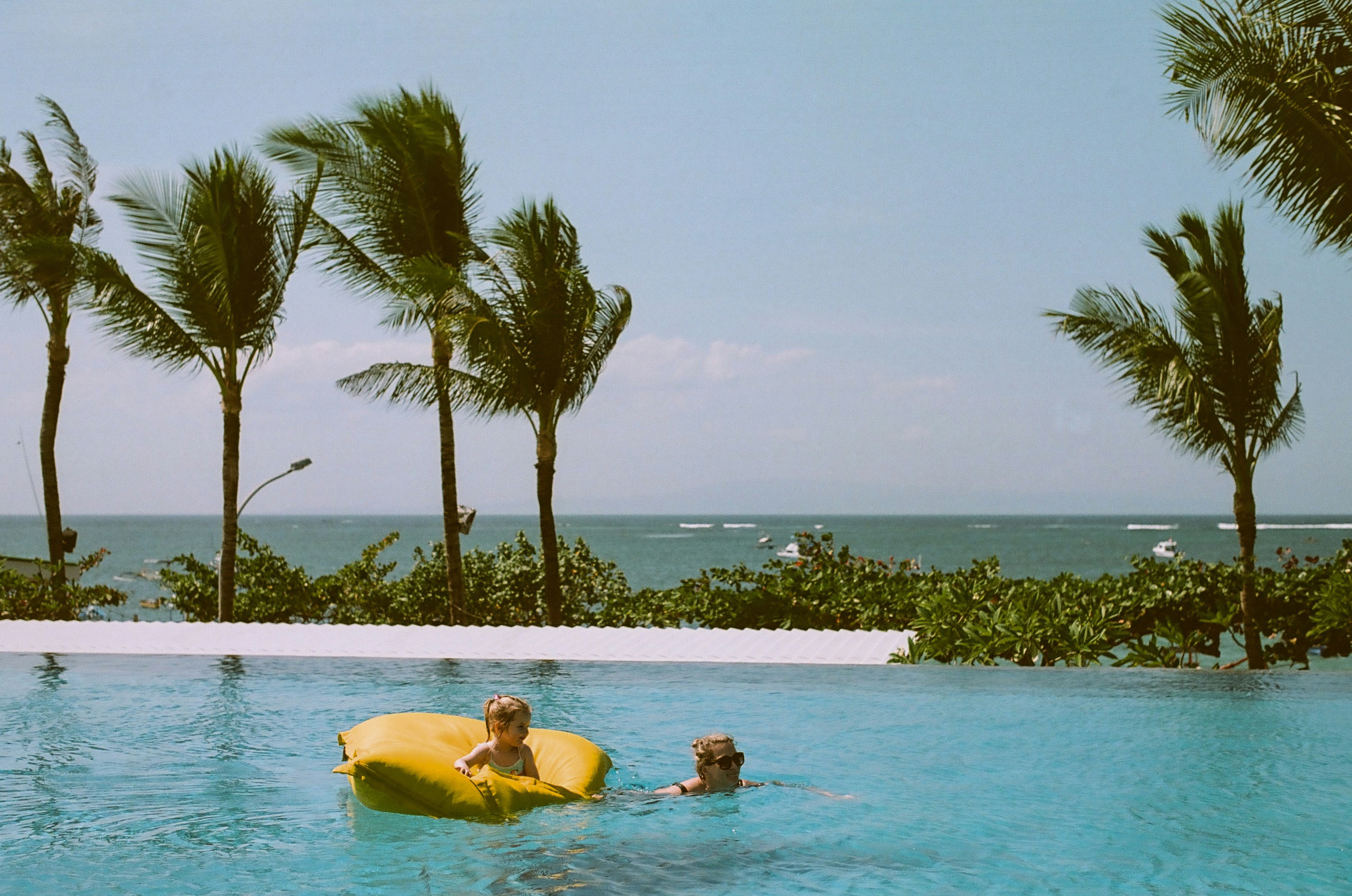 child on yellow pool float beside swimming woman