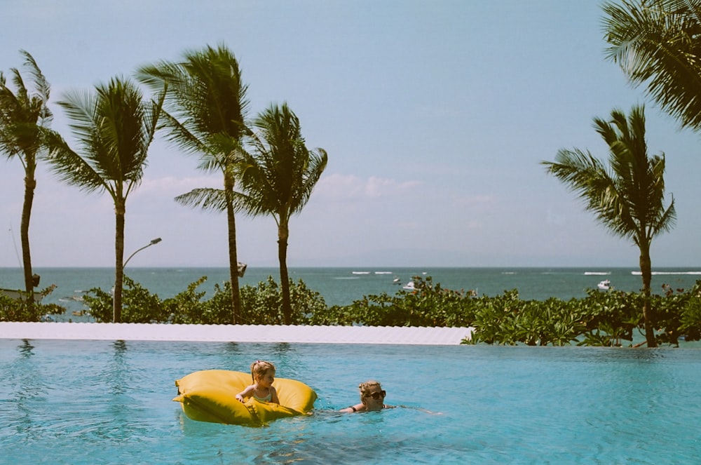 child on yellow pool float beside swimming woman