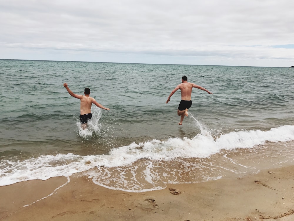 two man jumping on sea under blue sky during daytime