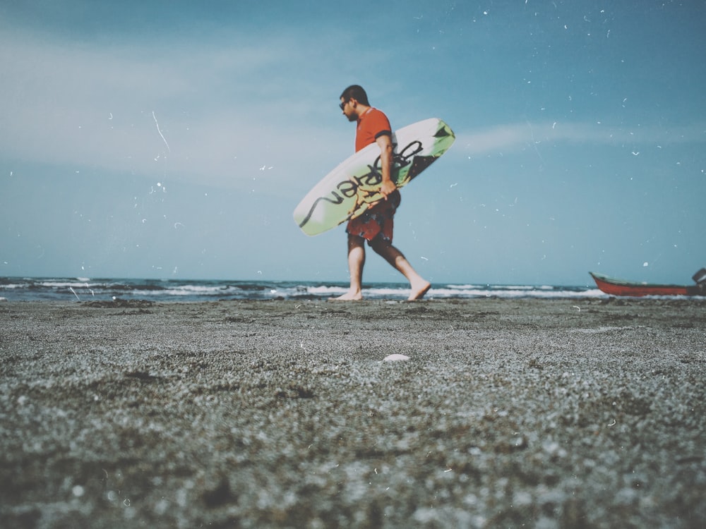 man in red t-shirt carrying surfboard at the shore