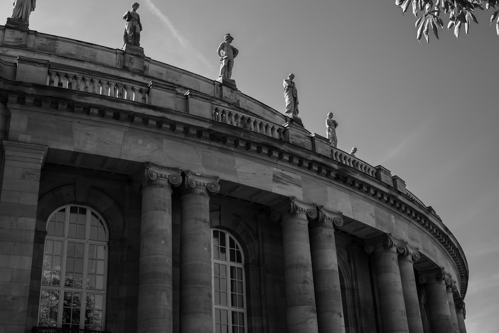 grayscale photo of concrete building with people standing statue on top