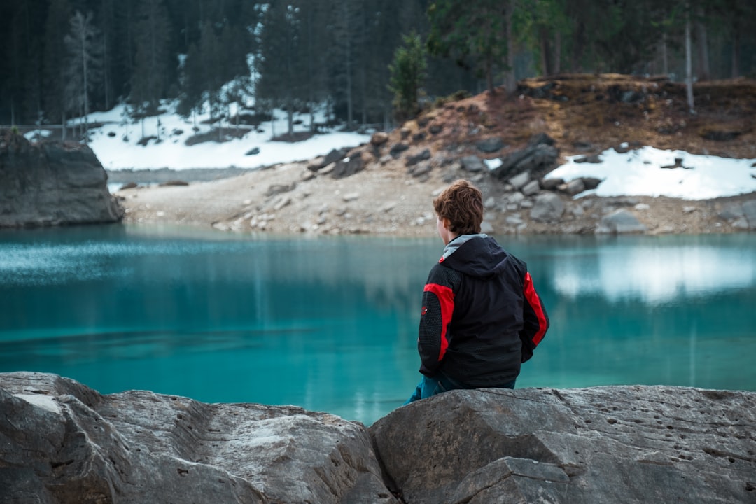 man sitting on rock looking straight on calm lake