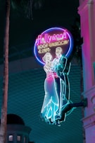 Brightly colored neon sign featuring a classical dancing couple silhouette. The sign reads 'Hollywood Roof Ballroom & Cafe' and exudes a retro, nostalgic vibe against a dark backdrop.