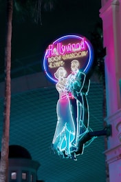 Brightly colored neon sign featuring a classical dancing couple silhouette. The sign reads 'Hollywood Roof Ballroom & Cafe' and exudes a retro, nostalgic vibe against a dark backdrop.