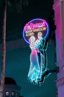 Brightly colored neon sign featuring a classical dancing couple silhouette. The sign reads 'Hollywood Roof Ballroom & Cafe' and exudes a retro, nostalgic vibe against a dark backdrop.