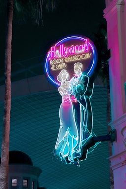 Brightly colored neon sign featuring a classical dancing couple silhouette. The sign reads 'Hollywood Roof Ballroom & Cafe' and exudes a retro, nostalgic vibe against a dark backdrop.