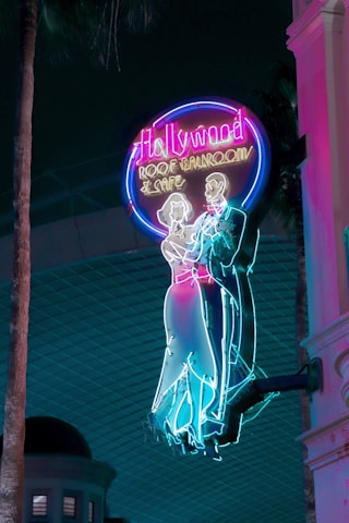 Brightly colored neon sign featuring a classical dancing couple silhouette. The sign reads 'Hollywood Roof Ballroom & Cafe' and exudes a retro, nostalgic vibe against a dark backdrop.