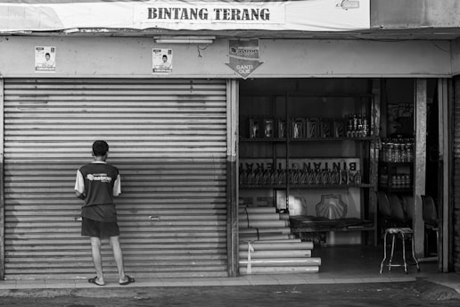 grayscale photo of man standing in front on closed roller shutter