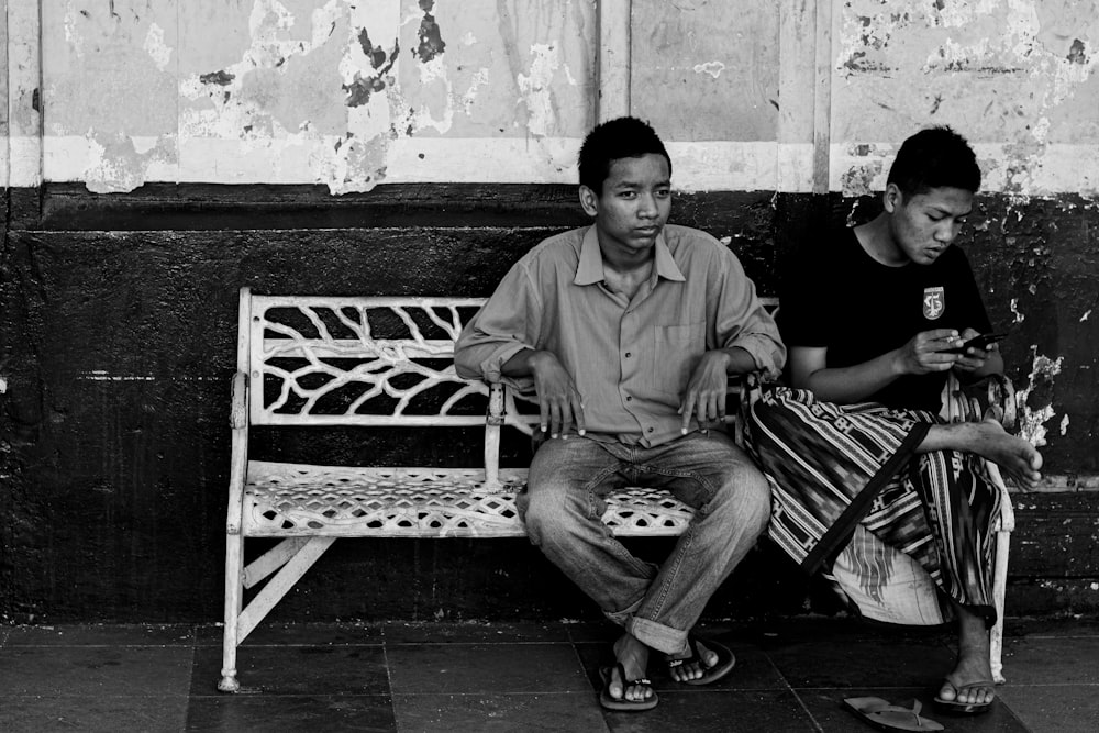 grayscale photo of two men sitting on bench