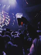 Live rock concert scene with fans raising beer bottles under colorful stage lights.