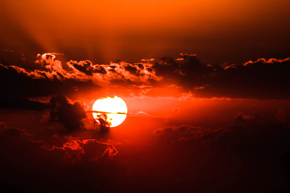 The image depicts a breathtaking sunset over a vast expanse of land, with the sun positioned low on the horizon and casting its warm glow across the sky. The sky is painted in hues of orange and red, creating a stunning backdrop for the setting sun. The clouds are scattered throughout the frame, adding depth to the scene. In the foreground, there's a large body of water that mirrors the vibrant colors of the sunset, enhancing the overall beauty of the image.