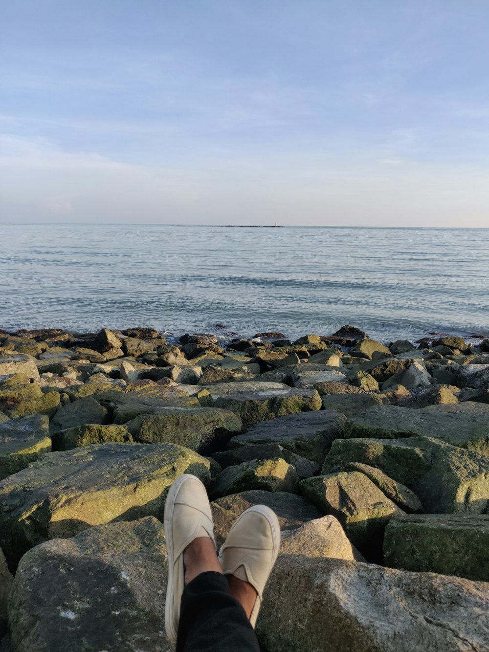 person sitting on rocks viewing calm sea