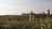 A serene landscape view with tall, slender grasses in the foreground and a gently rolling hillside in the background. The sky is clear, casting soft lighting over the green expanse.