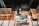 A person is working in a workshop, surrounded by various woodworking tools and materials. There are wooden panels, a measuring square, and a circular saw on the table. The floor is a rich brown wood, and beams of light create patterns on the surface.