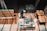 A person is working in a workshop, surrounded by various woodworking tools and materials. There are wooden panels, a measuring square, and a circular saw on the table. The floor is a rich brown wood, and beams of light create patterns on the surface.