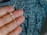 A hand holding a silver necklace with a crucifix pendant. The background is a textured fabric with shades of blue and black.
