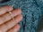 A hand holding a silver necklace with a crucifix pendant. The background is a textured fabric with shades of blue and black.