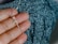 A hand holding a silver necklace with a crucifix pendant. The background is a textured fabric with shades of blue and black.