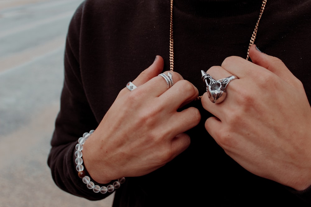 person wearing silver-colored rings holding gold-colored necklace