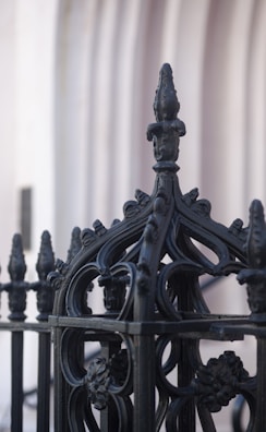 A black wrought iron fence with decorative finials surrounding a suburban home.